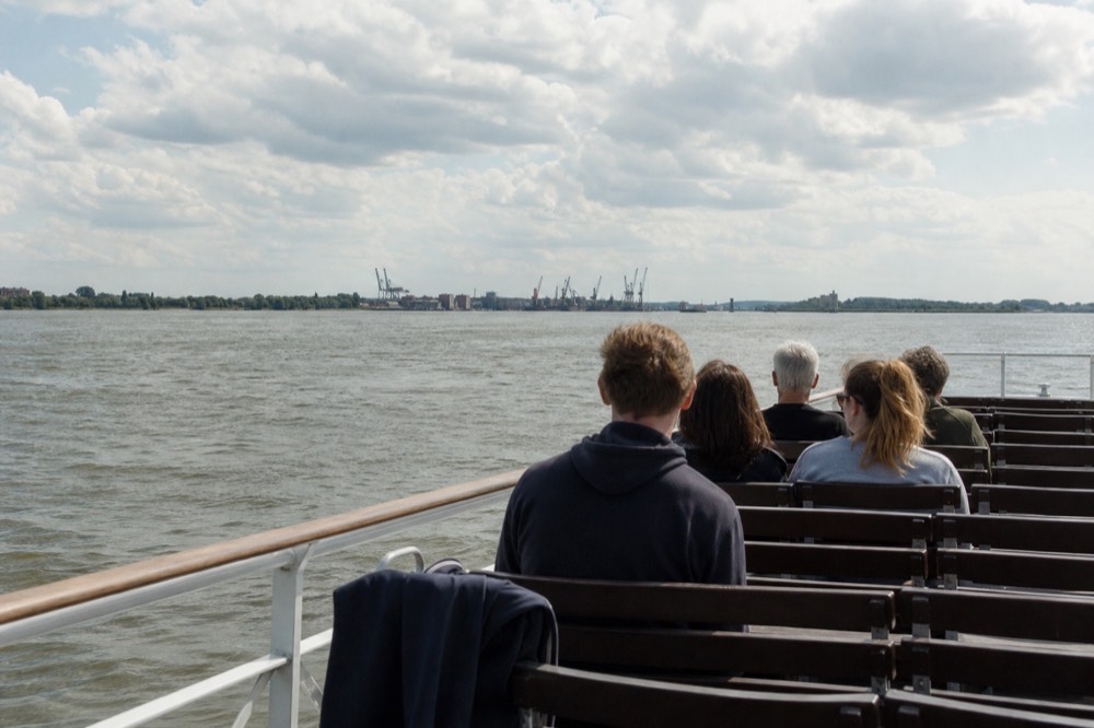 A small tour boat on the Savannah River with cargo cranes in the distance, no text, no logos, no people