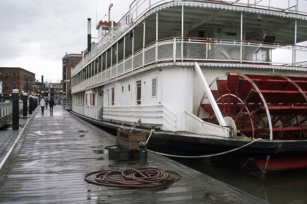 A paddlewheel riverboat docked on River Street with the Savannah waterfront behind it, no text, no logos, no people