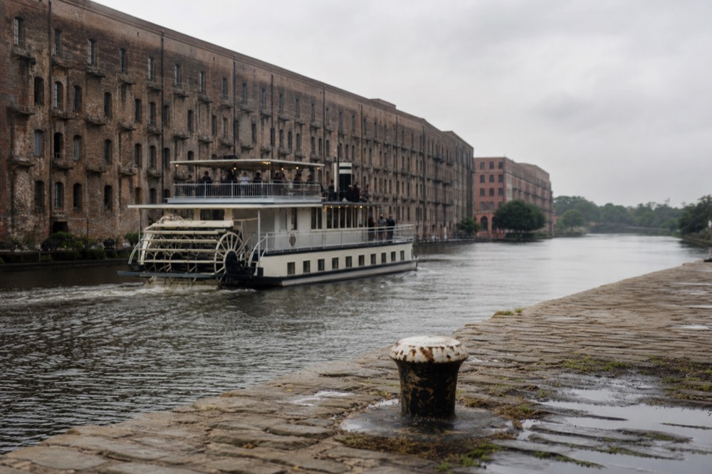 A paddlewheel riverboat cruising past River Street's historic cotton warehouses, no text, no logos, no people