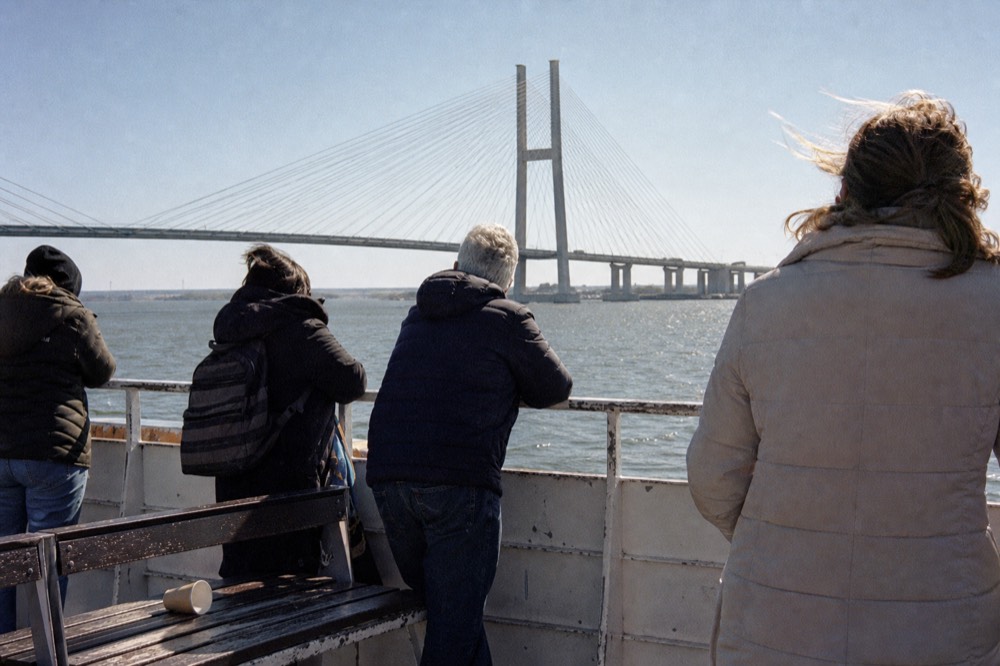 Passengers on an open-air riverboat deck looking out toward the Talmadge Bridge, no text, no logos, no people
