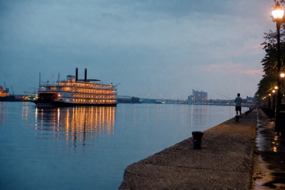 A riverboat on calm water at dusk with warm light on the river surface, no text, no logos, no people