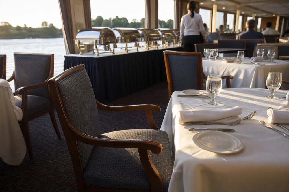 Dining room on the riverboat with tables set for dinner and buffet station in the background, no text, no logos, no people