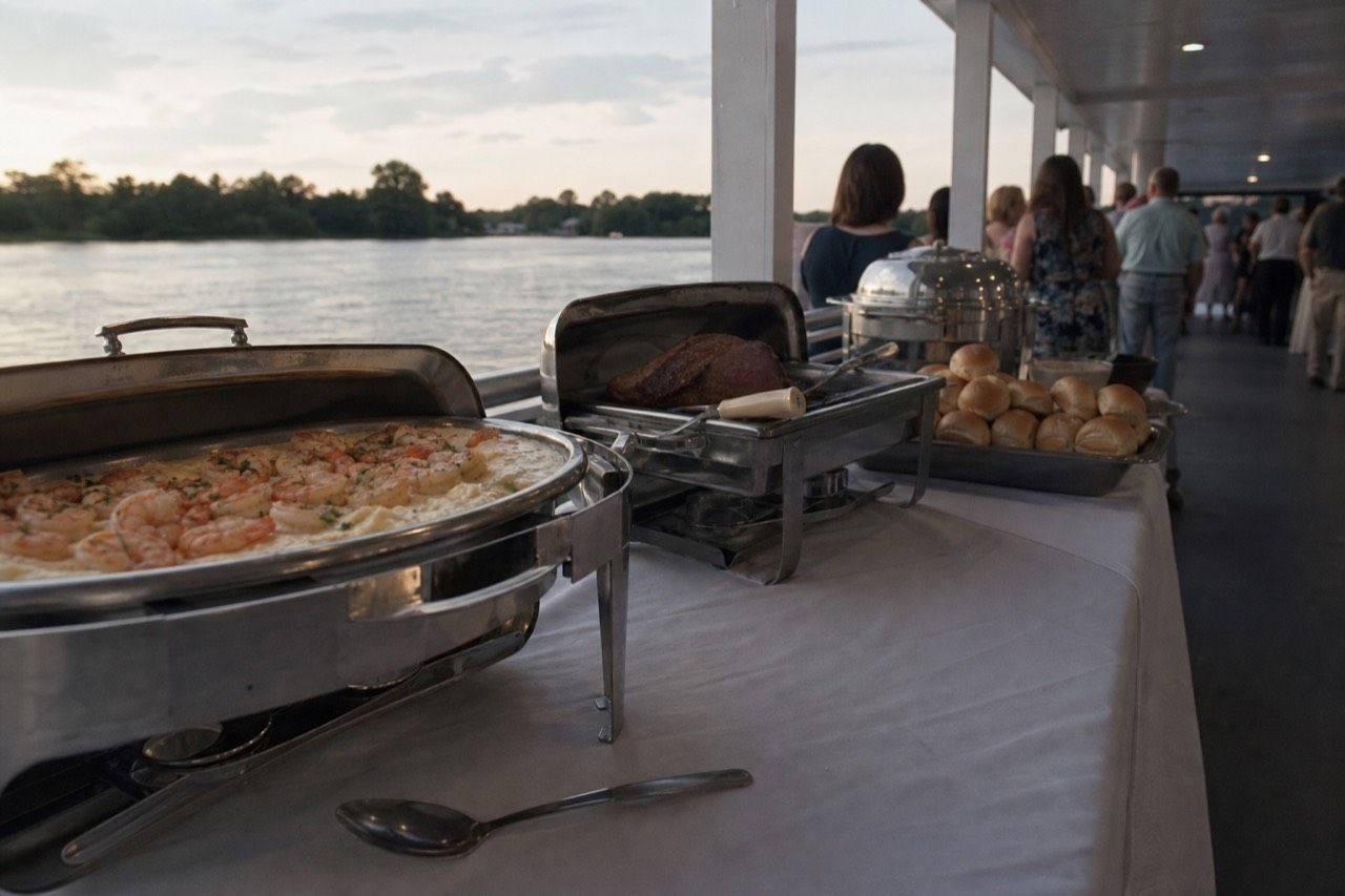Southern dinner buffet with shrimp and grits, roast beef carving station, and warm sides on a riverboat, no text, no logos, no people