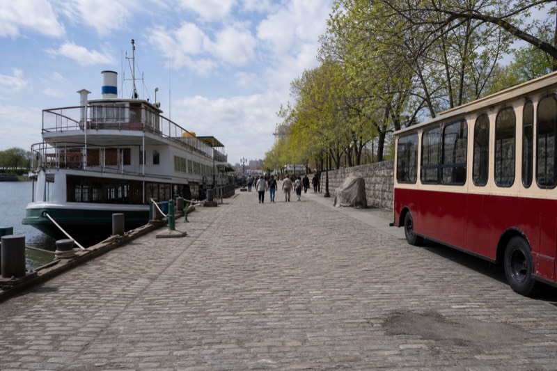 A riverboat docked on River Street beside a historic trolley on the cobblestone waterfront in Savannah
