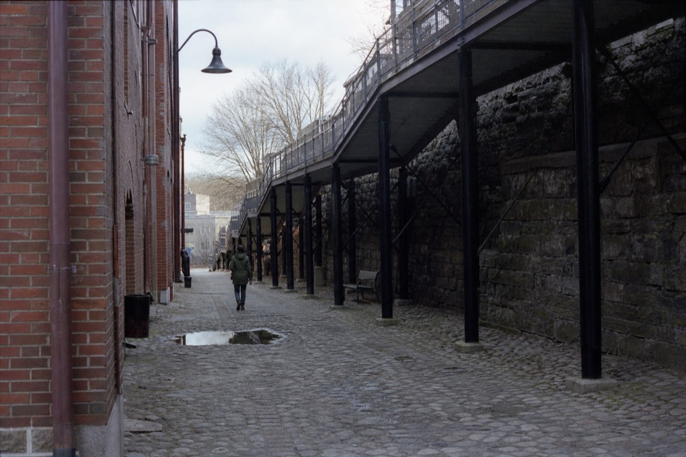 Cobblestone promenade along old brick warehouses with iron ramps climbing the bluff, no text, no logos, no people