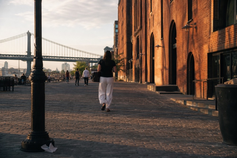 Golden light on cobblestones and brick warehouse facades with the river and bridge behind, no text, no logos, no people