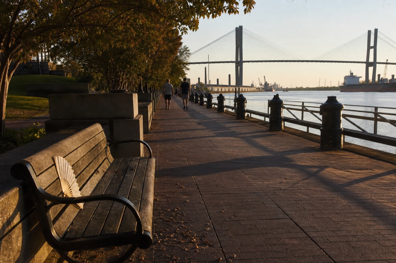 Savannah riverfront promenade at golden hour with the Talmadge Bridge in the distance, no text, no logos, no people.