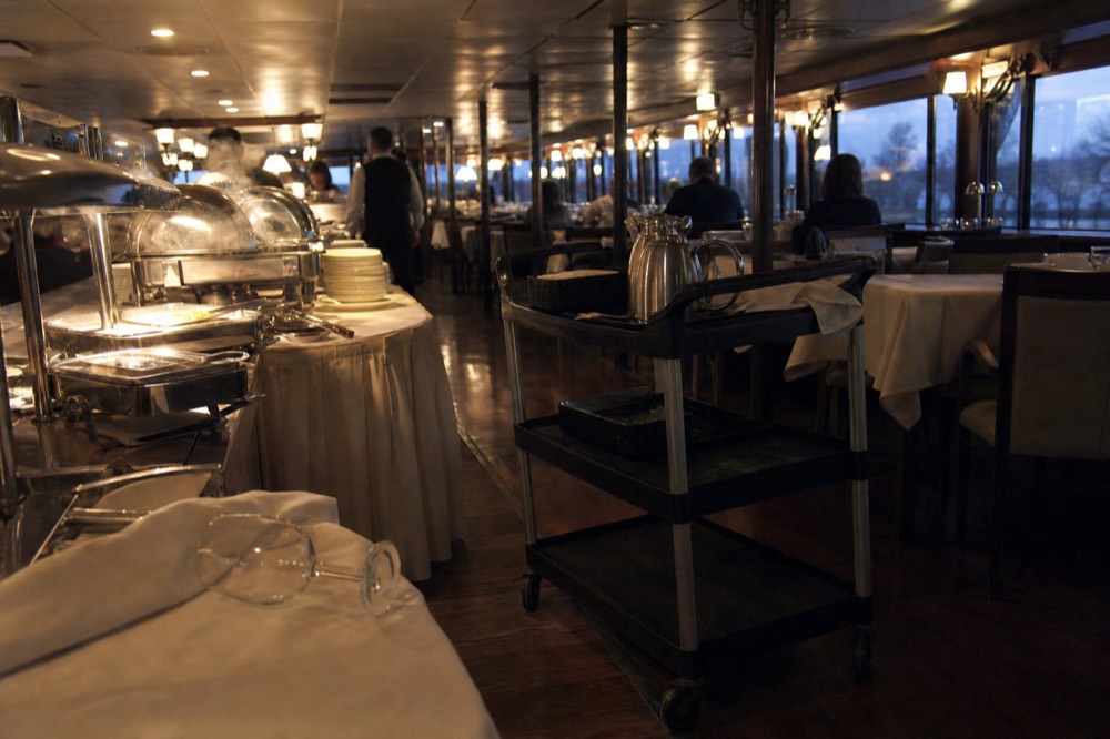 A dining deck set with buffet stations and warm lamplight aboard a riverboat, no text, no logos, no people