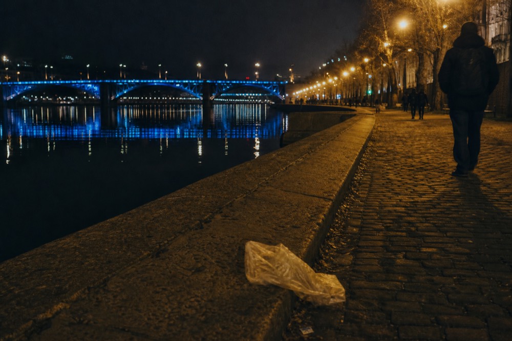 A riverfront at night with warm streetlights along the water and a lit bridge beyond, no text, no logos, no people