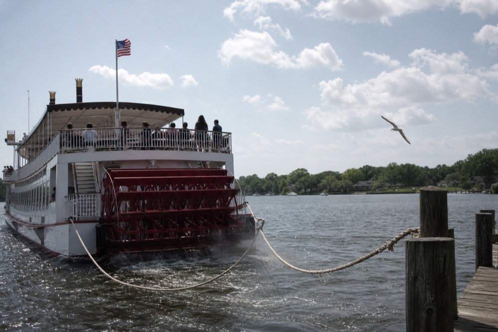 A riverboat pulling away from the River Street dock midday with passengers on the open upper deck, no text, no logos, no people