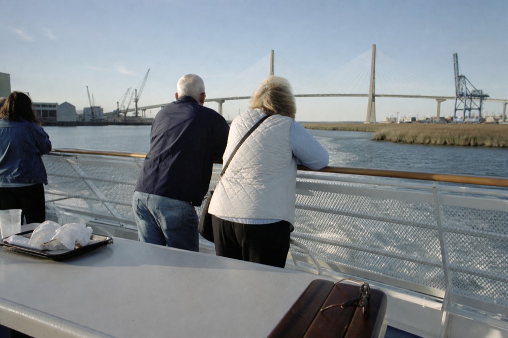 Passengers on a riverboat upper deck watching the Savannah harbor pass by in daylight, no text, no logos, no people