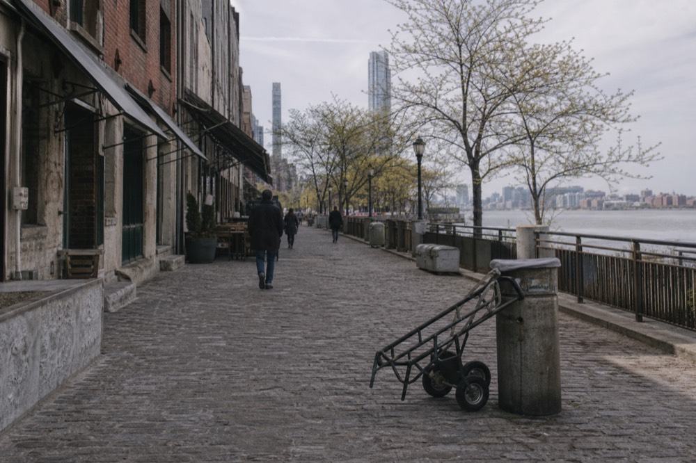 The cobblestone stretch of River Street with shops and the riverfront plaza in midday light, no text, no logos, no people