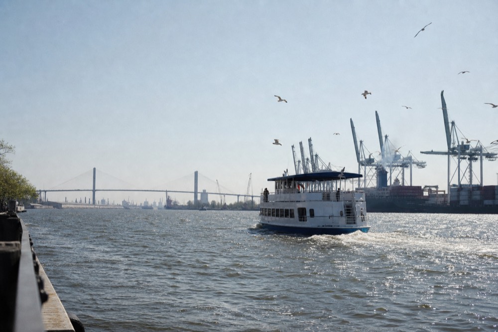 Riverboat cruising past the Savannah waterfront with the Talmadge Bridge in the distance, no text, no logos, no people