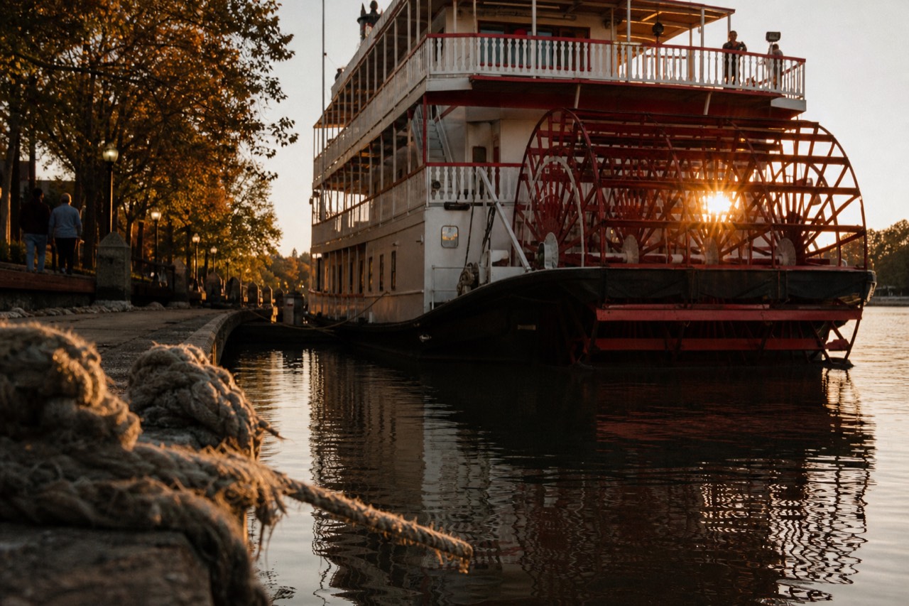 A red and white paddlewheel riverboat docked on the Savannah River at golden hour, no text, no logos, no people