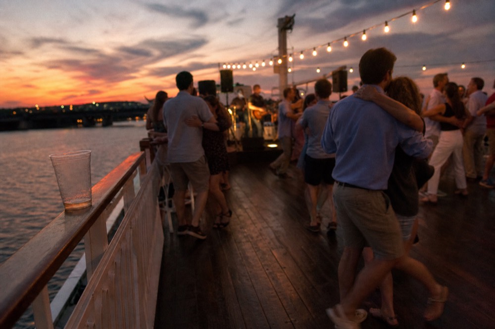 Passengers dancing near a live band on a riverboat deck at sunset, no text, no logos, no people