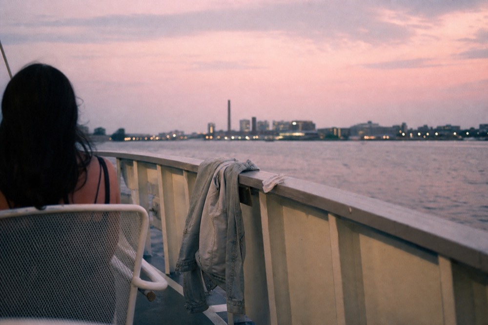A jacket draped over a deck rail on a riverboat with the sky turning pink over the river, no text, no logos, no people