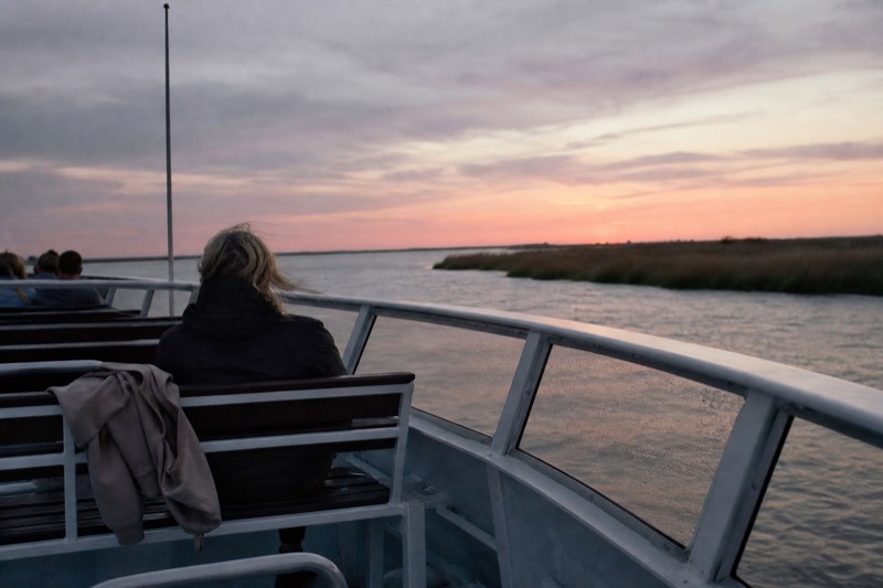 Passengers along the rail of a Savannah riverboat as the sky turns orange over the river at sunset, departing from the historic River Street waterfront in downtown Savannah