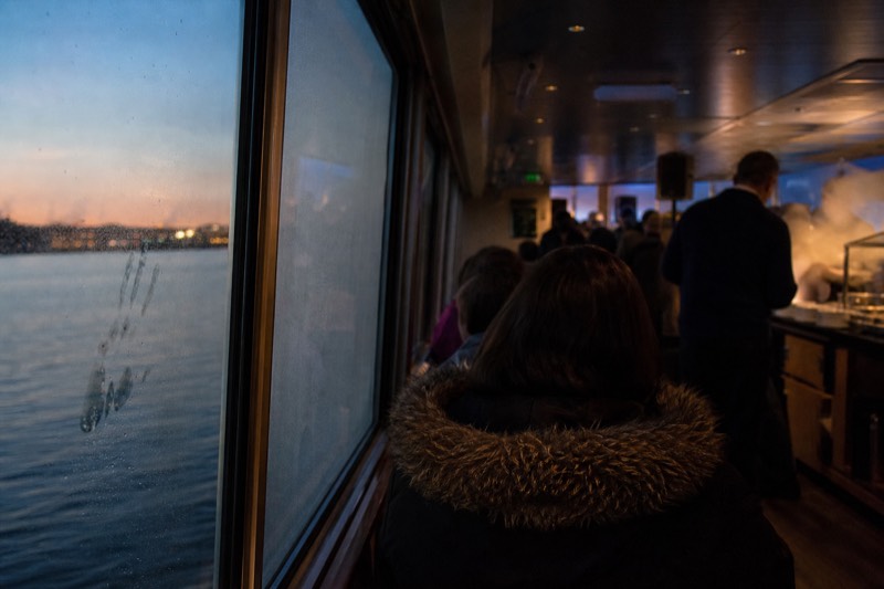 Dinner tables set on the covered deck of a Savannah riverboat at dusk, city lights reflecting on the Savannah River, departing from the historic River Street waterfront in downtown Savannah