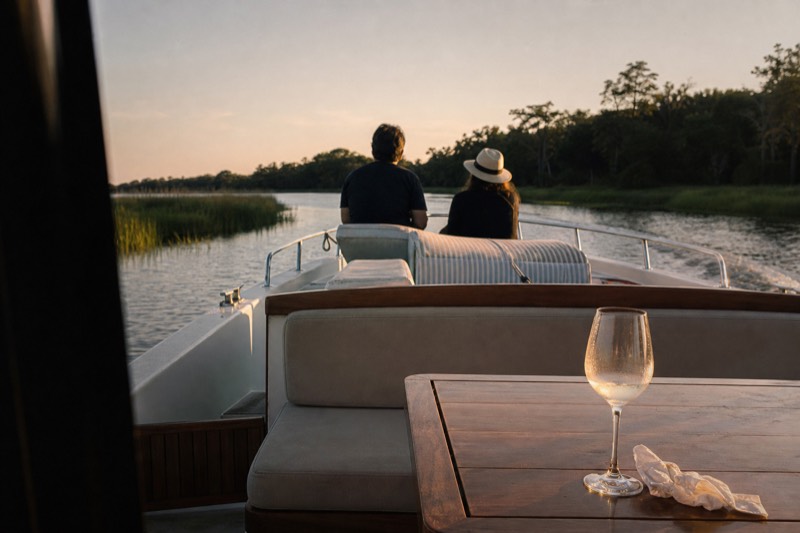 A small private charter boat idling on the Savannah River near the Hutchinson Island shoreline at golden hour, departing near the Savannah Convention Center on the river's north bank